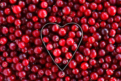 Background of ripe cranberries in the shape of a metal heart. cranberry texture close-up. autumn 