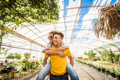 Teenage boy piggybacking mother in greenhouse