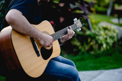 Midsection of man playing guitar outdoors