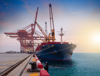 Cranes at commercial dock against sky during sunset