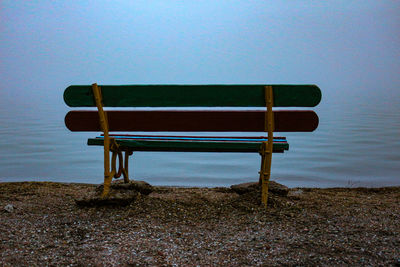 Empty bench on beach against clear sky