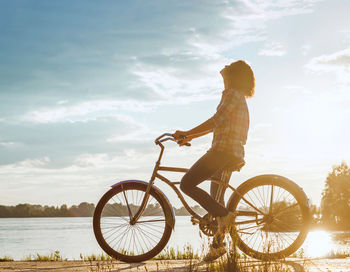 Rear view of man riding bicycle by lake against sky