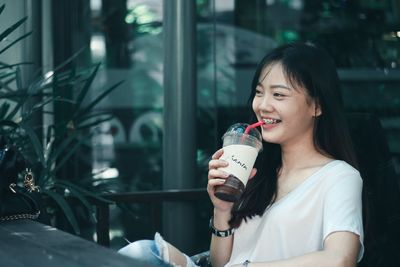 Young woman drinking glass while sitting outdoors