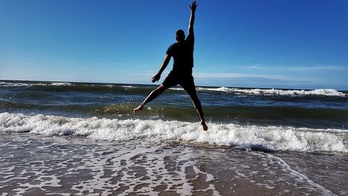 Rear view of man jumping on shore at beach against sky