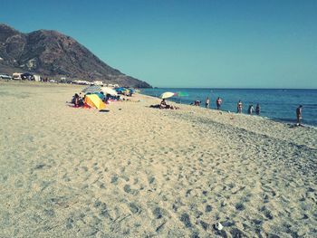 People enjoying at beach against clear blue sky