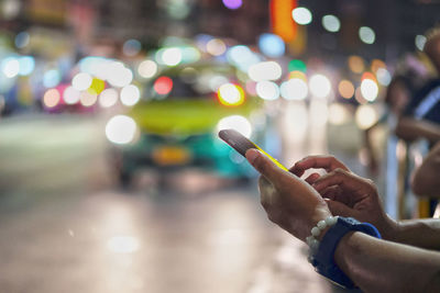 Cropped hands of man using mobile phone in illuminated city at night