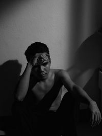 Portrait of young man sitting against wall at home