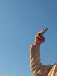 Low angle view of hand holding smart phone against clear sky