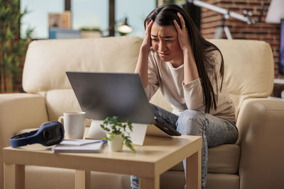 Businesswoman using laptop while sitting on sofa at home