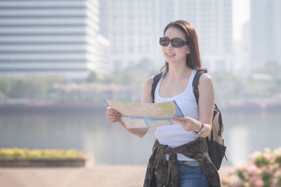 Young woman wearing sunglasses standing against city in background