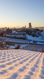 Snow covered field by lake against sky during sunset