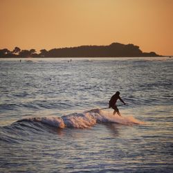 Silhouette man paddleboarding on sea against sky during sunset