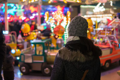 Rear view of woman against illuminated rides at night