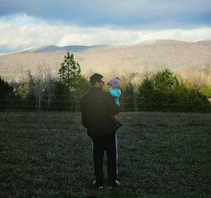 Man standing on field against cloudy sky