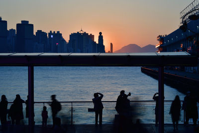 Silhouette people by sea against sky during sunset