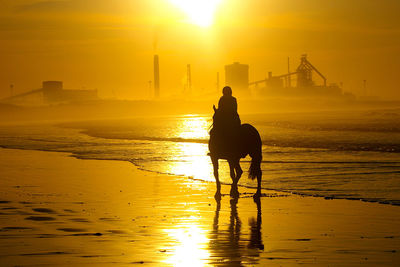 Rear view of silhouette man riding woman on sea during sunset