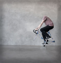 Digital composite image of man riding damaged bicycle against wall