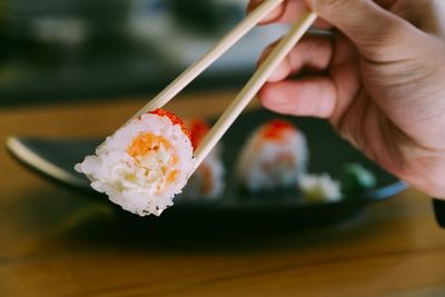 Cropped hand of person having sushi with chopsticks on table