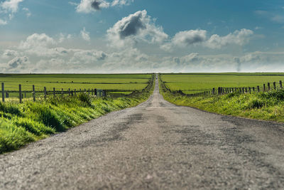 Surface level of road amidst field against sky