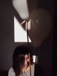 Happy woman holding balloons against wall at home