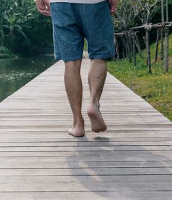 Low section of man walking on wooden pier