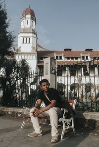 Portrait of young man sitting against building in city