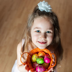 Caucasian girl holding multicolored chocolate eggs in a basket and looking upwards into the camera