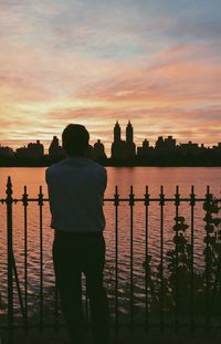 Rear view of silhouette man standing on railing against sea