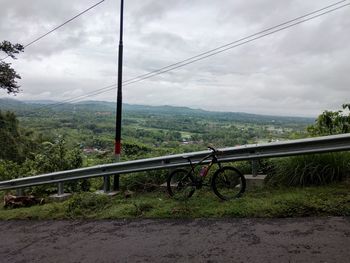 Bicycle by railing on mountain against sky