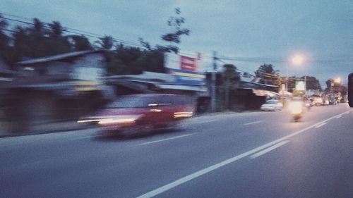 Cars on road by illuminated city against sky