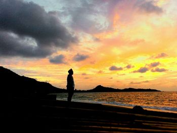 Silhouette man overlooking calm lake at sunset