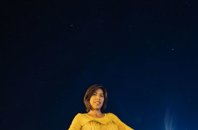 Portrait of smiling woman against blue sky at night