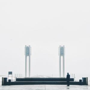 Rear view of man standing by skyscraper against clear sky