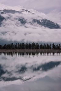 Scenic view of mountain, trees, and low clouds reflected in lake 