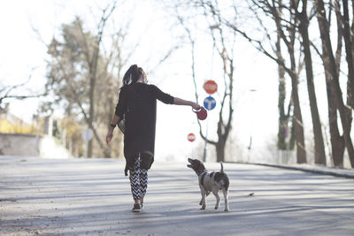 Rear view of woman with dog walking on road