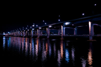 Illuminated bridge over river against sky at night