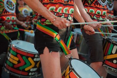 Woman in brightly patterned clothes and black shorts playing steel drums during a street festival.