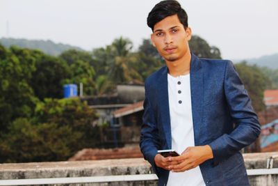 Portrait of young man holding mobile phone against sky