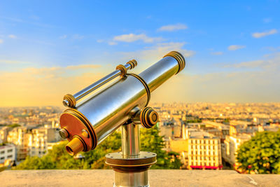 Coin-operated binoculars against buildings in city against sky