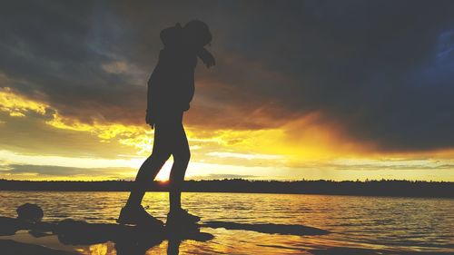 Silhouette woman standing by sea against sky during sunset