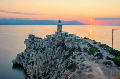 Lighthouse by sea against sky during sunset