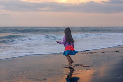 Side view of girl running at beach during sunset