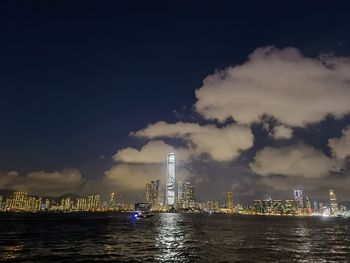 Illuminated buildings by river against sky at night