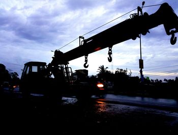 Silhouette cranes at construction site against sky during sunset