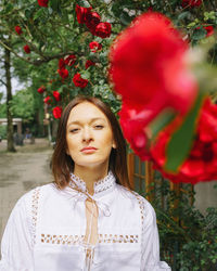 Portrait of young woman standing against roses 