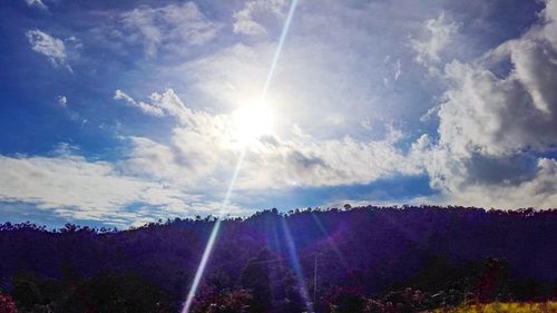 Low angle view of sunlight streaming through clouds