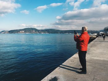 Rear view of woman standing by lake against sky