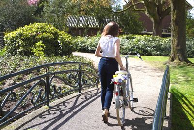 Full length rear view of woman walking with bicycle over footbridge