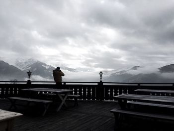 Silhouette man standing by railing against cloudy sky