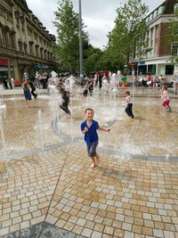 People at wet shore against sky in city